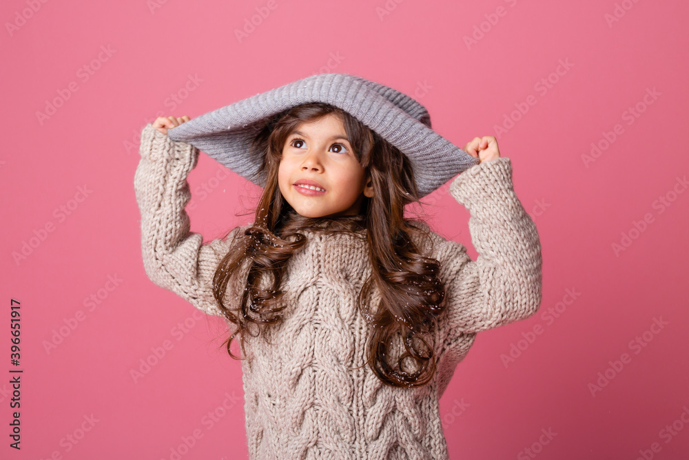 little brunette girl with long hair in winter clothes on a pink background in the Studio. knitwear for children, space for text little brunette girl with long hair in winter clothes on a pink background in the Studio. knitwear for children, space for text