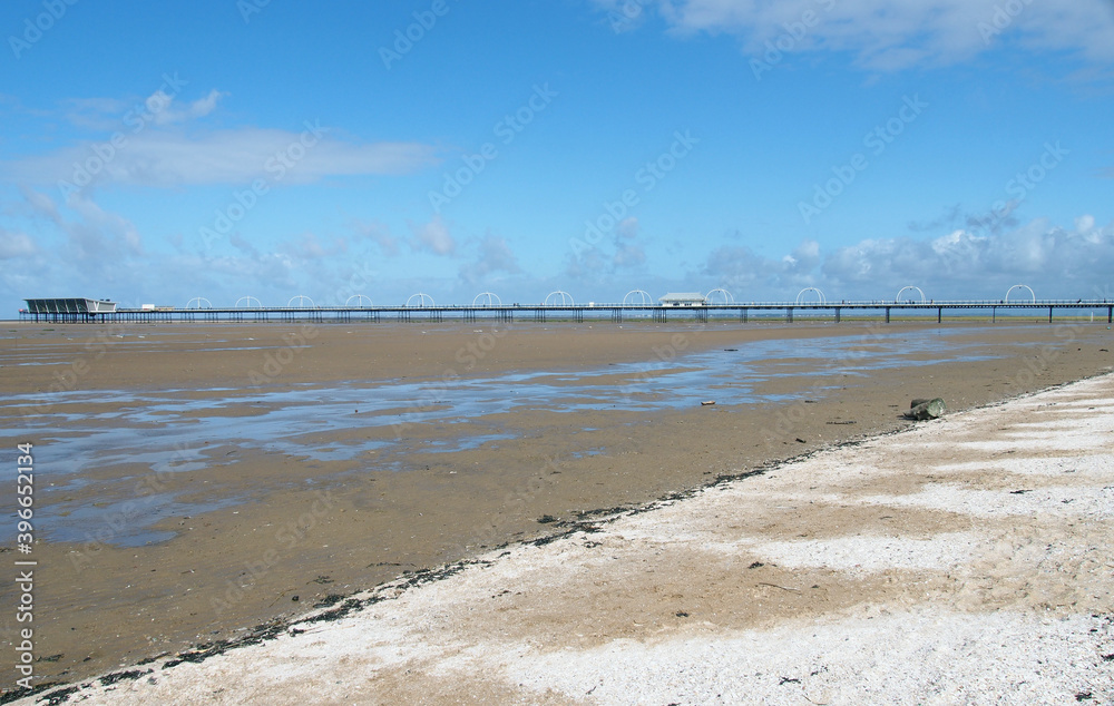 the historic pier at southport merseyside with the beach at low tide and summer sky reflected in water on the beach