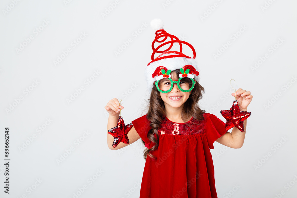 funny little girl in a Santa hat and glasses holding Christmas toys on a white background of isolate. the concept of Christmas, the space for text