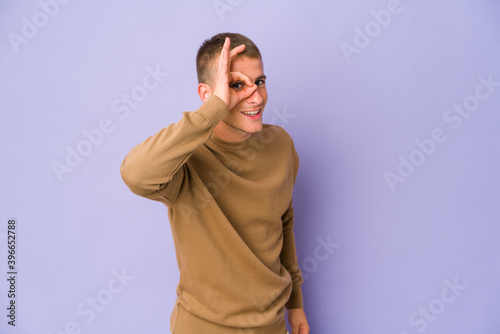 Young caucasian handsome man excited keeping ok gesture on eye.