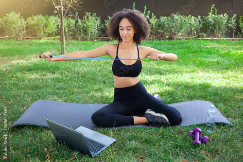 Snapshot of attractive and skinny African-American girl sitting in the open air, studying online all details of working with the rope. Sport, healthcare and technology concept.