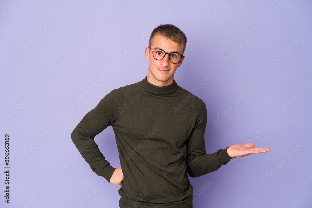 Young caucasian handsome man showing a copy space on a palm and holding another hand on waist.