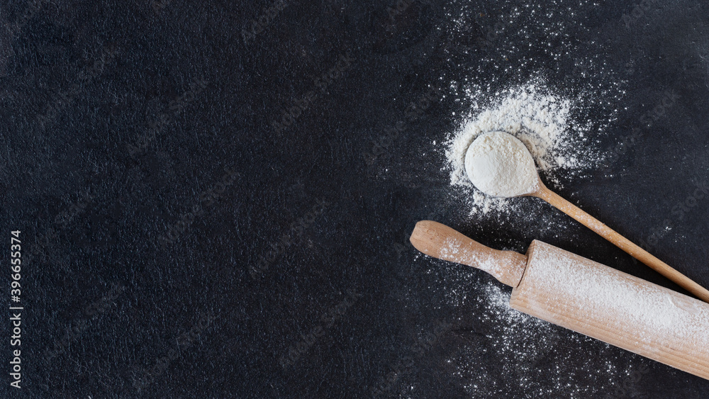 Wheat flour in a wooden spoon with rolling pin over black surface top view. Wheat flour in a wooden spoon with rolling pin over black surface top view.