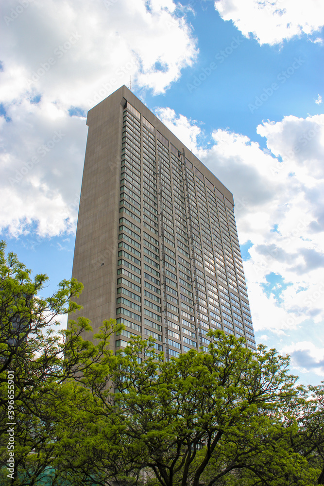 Tall office building in the city with green trees at the base and blue cloudy sky