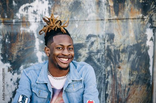 Handsome African-American Young man wearing a denim jacket with dreadlocks and facial hair and looking at the camera and smiling photo