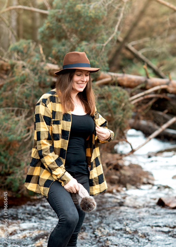 Happy woman in yellow shirt and hat walking along the river in the autumn forest