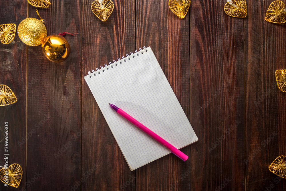 Notepad and pink pen on a wooden table with Christmas balls and a garland. Flatlay Notepad and pink pen on a wooden table with Christmas balls and a garland. Flatlay