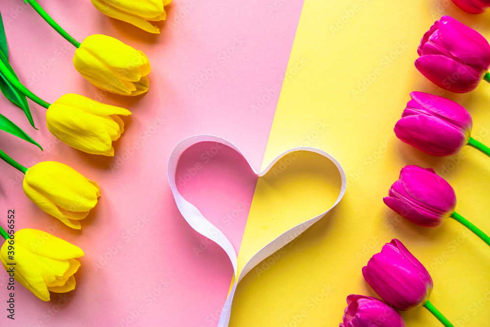 Fresh tulips flowers with heart on delicate pastel light pink and yellow background. Valentine's Day, Mother's or Woman's Day greeting cards. Fresh tulips flowers with heart on delicate pastel light pink and yellow background. Valentine's Day, Mother's or Woman's Day greeting cards.