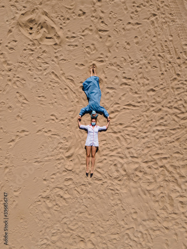 Funny: Two female doctors in medical gear make sand angels lying on beach