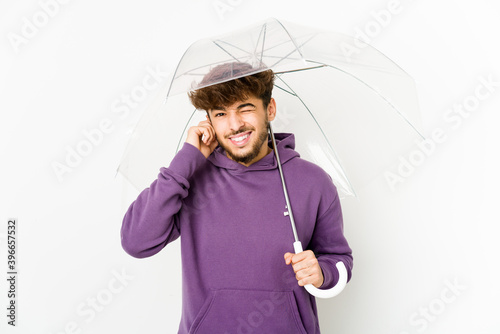 Young arab man holding an umbrella covering ears with hands.