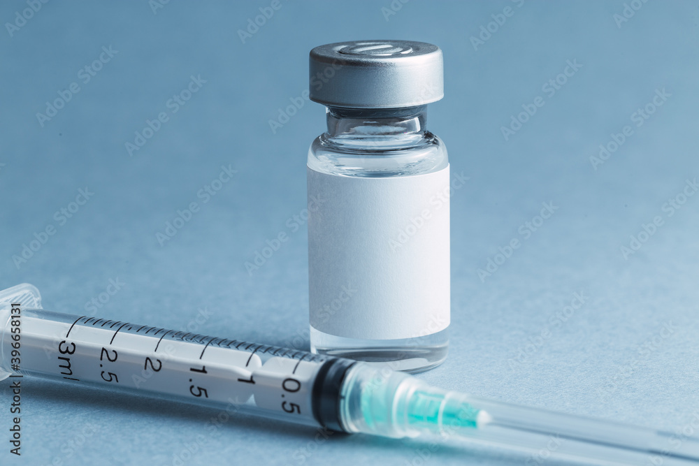 A glass vial of a medical drug vaccine next to a sterile hypodermic syringe A glass vial of a medical drug vaccine next to a sterile hypodermic syringe