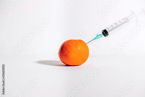 Syringe giving a prick to a tangerine on white background. Medical concept. Copy space.