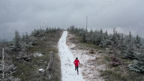 Aerial video on a woman runner in a red sweatshirt runs on a mountain trail in a winter landscape.
