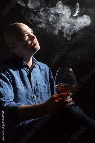Solid bald man in shirt with glass of whisky and fume studio portrait.