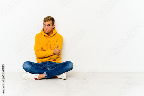 Young caucasian man sitting on the floor suspicious, uncertain, examining you. © Asier