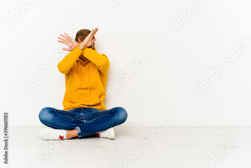 Young caucasian man sitting on the floor keeping two arms crossed, denial concept.