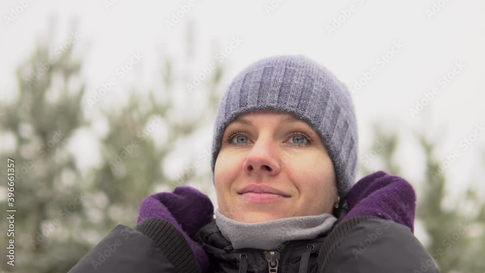 Portrait of a young beautiful woman in purple mittens who straightens her hat. Outdoors in winter.Close-up Portrait of a young beautiful woman in purple mittens who straightens her hat. Outdoors in winter.Close-up