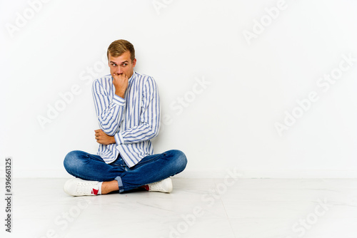 Young caucasian man sitting on the floor biting fingernails, nervous and very anxious. © Asier