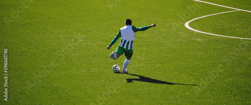 Futebol - jogador com equipamento verde e branco a chutar a bola na zona do meio campo fora da grande área - relvado artificial photo