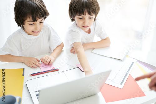 Two adorable latin boys, brothers looking focused, sitting together at the table, looking at the screen of laptop. Little kids having online lesson at home