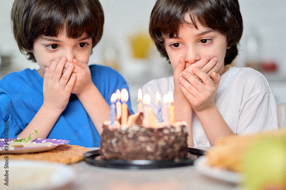 Magic moment. Adorable little hispanic boys looking at birthday cake, making wishes while getting ready for blowing candles Magic moment. Adorable little hispanic boys looking at birthday cake, making wishes while getting ready for blowing candles