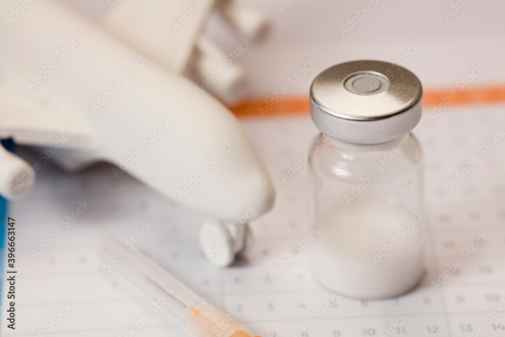 Glass vaccine vial, with syringe, and plane, in calendar 2021