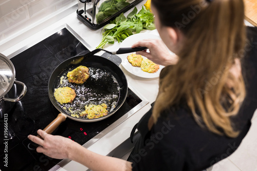 Young charming Swedish woman cooking at home in her kitchen, preparing healthy mediterranean food for her family. Young food blogger doing food preparation in her kitchen, frying vegetables