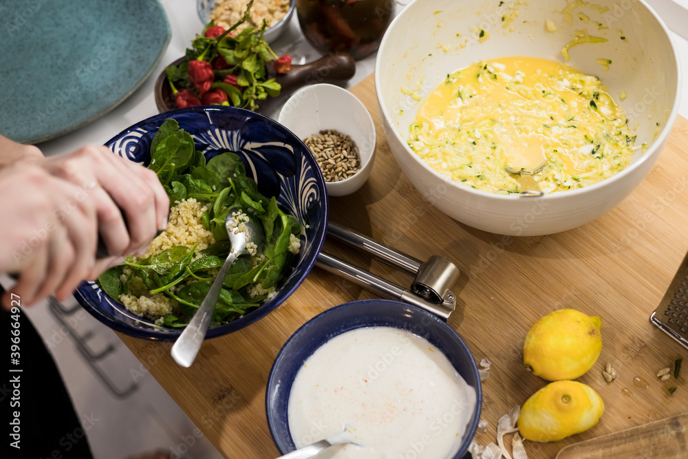 Close up of woman hands garnishing a fresh vegetarian salad with cous cous. Woman cooking in the kitchen at home preparing healthy food. Mediterranean cusine concept.