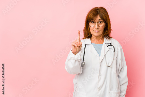 Middle age caucasian doctor woman isolated showing number one with finger.