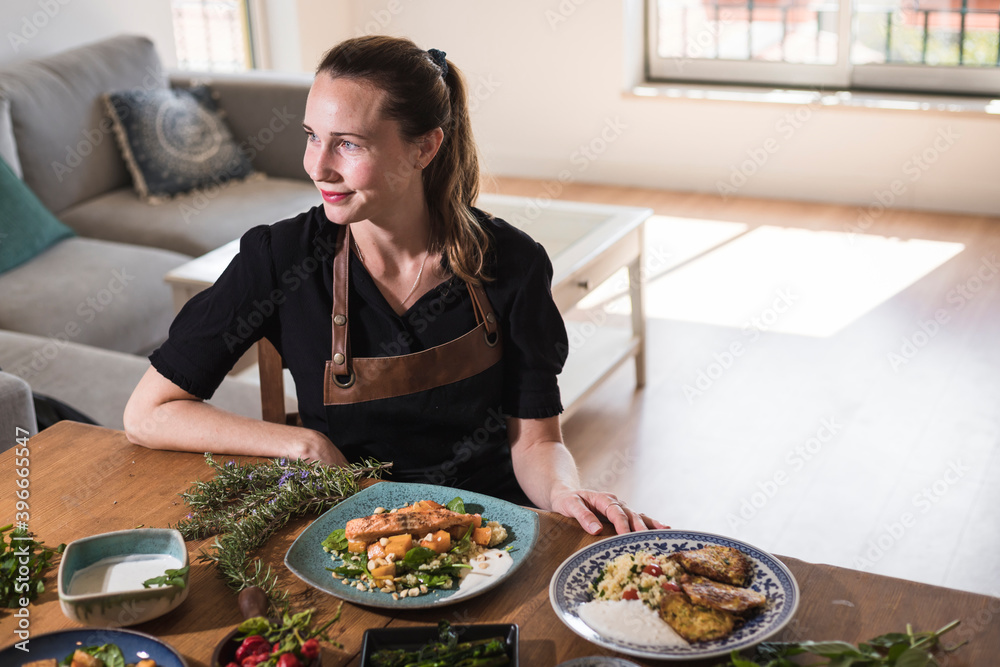 Young attractive swedish food blogger posing in front of a table full of food dishes. Young girl sitting in front of a wooden table eating vegetarian food and healthy dishes. Vegetarian lifestyle