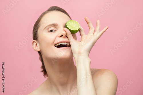 Beautiful sensual topless brunette woman standing isolated over pink background and hold lime in hand