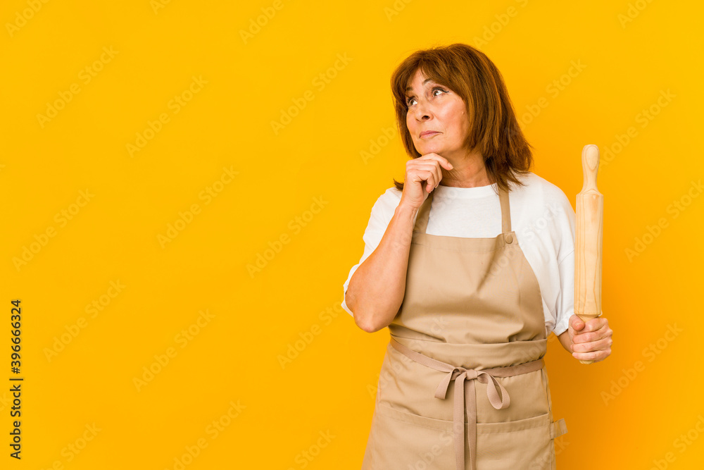 Middle age caucasian cook woman holding a roller isolated looking sideways with doubtful and skeptical expression. Middle age caucasian cook woman holding a roller isolated looking sideways with doubtful and skeptical expression.