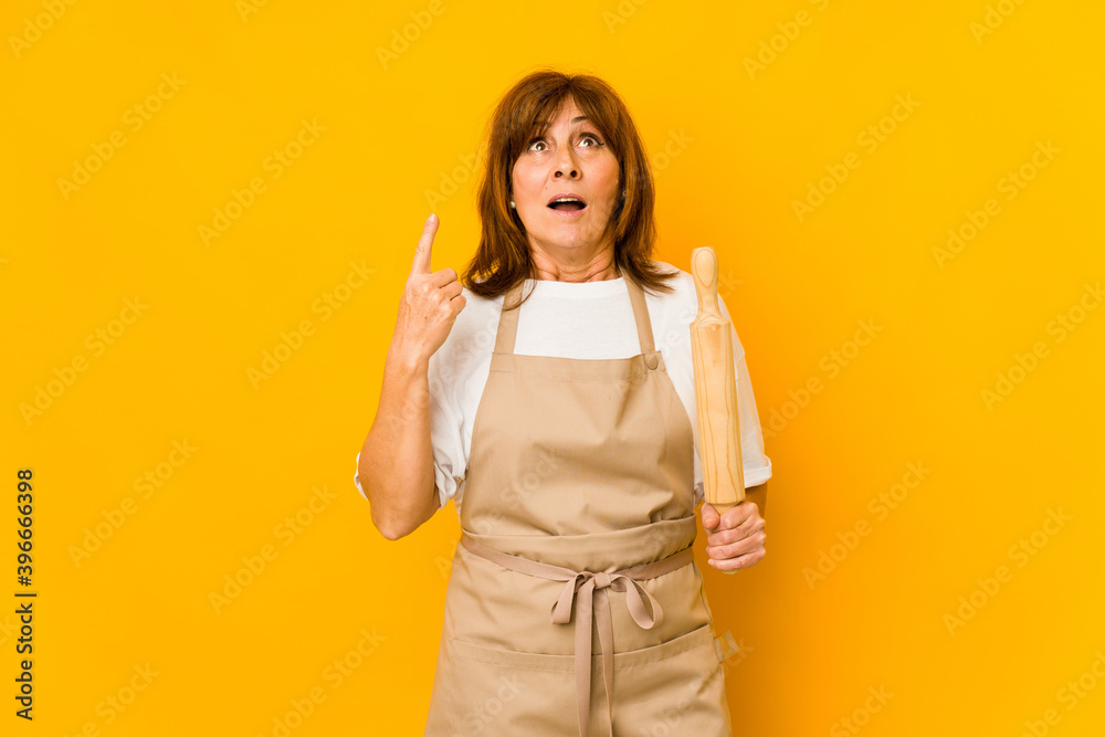 Middle age caucasian cook woman holding a roller isolated pointing upside with opened mouth. Middle age caucasian cook woman holding a roller isolated pointing upside with opened mouth.