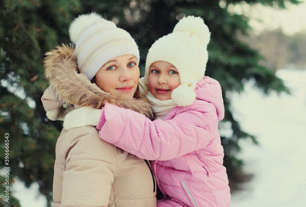 Portrait of happy smiling mother and little child in winter day over snowy christmas tree background