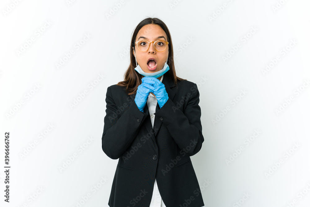 Young business latin woman wearing a mask to protect from covid isolated on white background praying for luck, amazed and opening mouth looking to front. Young business latin woman wearing a mask to protect from covid isolated on white background praying for luck, amazed and opening mouth looking to front.