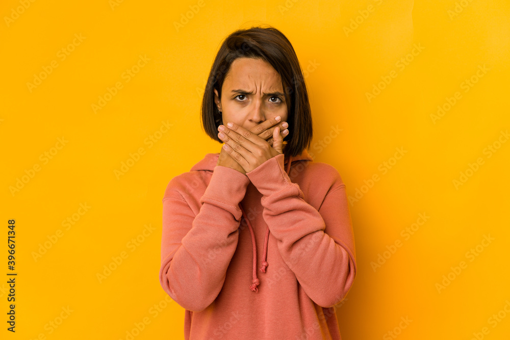 Young hispanic woman isolated on yellow covering mouth with hands looking worried.