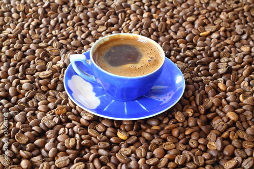 Close-up and top view of hot black coffee in blue coffee cup and roasted Thai coffee beans on wooden background. photo