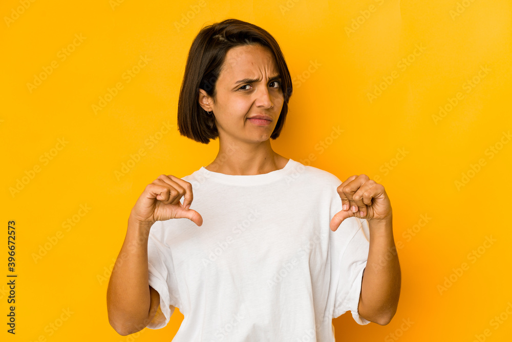 Young hispanic woman isolated on yellow showing thumb down, disappointment concept. Young hispanic woman isolated on yellow showing thumb down, disappointment concept.