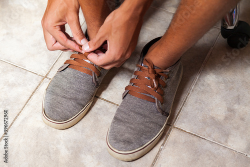 Detail of the hands of a young Brazilian man tying the tennis shoe to practice walking in the neighborhood. Footwear concept. Sport concept.