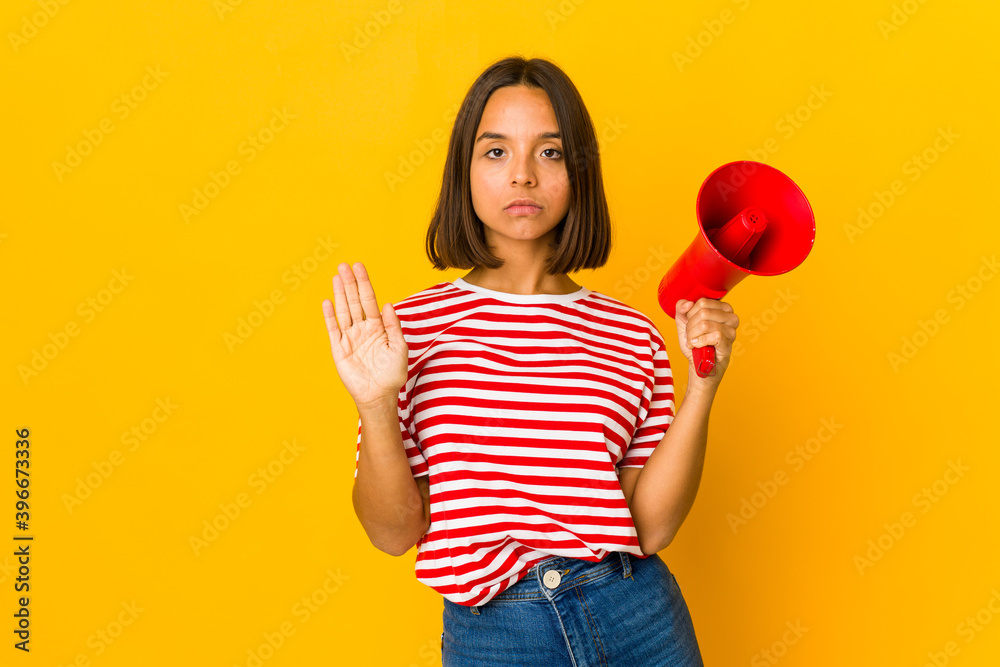 Young hispanic woman holding a megaphone standing with outstretched hand showing stop sign, preventing you. Young hispanic woman holding a megaphone standing with outstretched hand showing stop sign, preventing you.