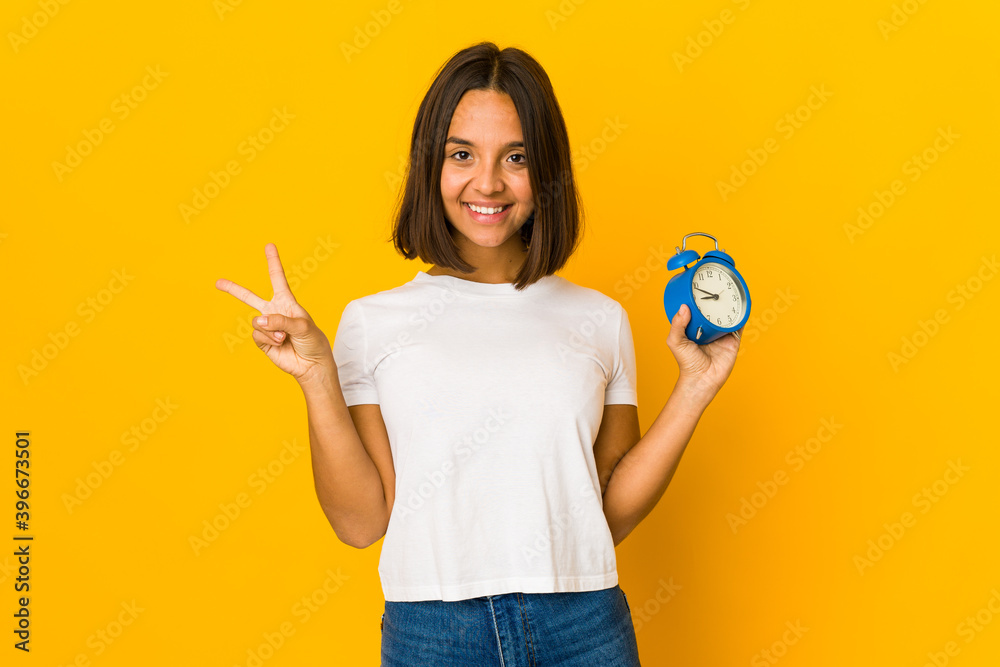Young hispanic woman holding a megaphone joyful and carefree showing a peace symbol with fingers. Young hispanic woman holding a megaphone joyful and carefree showing a peace symbol with fingers.