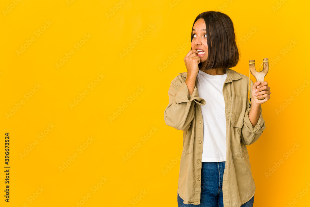 Young hispanic woman holding a slingshot relaxed thinking about something looking at a copy space. Young hispanic woman holding a slingshot relaxed thinking about something looking at a copy space.