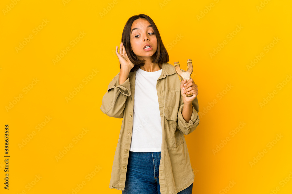 Young hispanic woman holding a slingshot trying to listening a gossip. Young hispanic woman holding a slingshot trying to listening a gossip.
