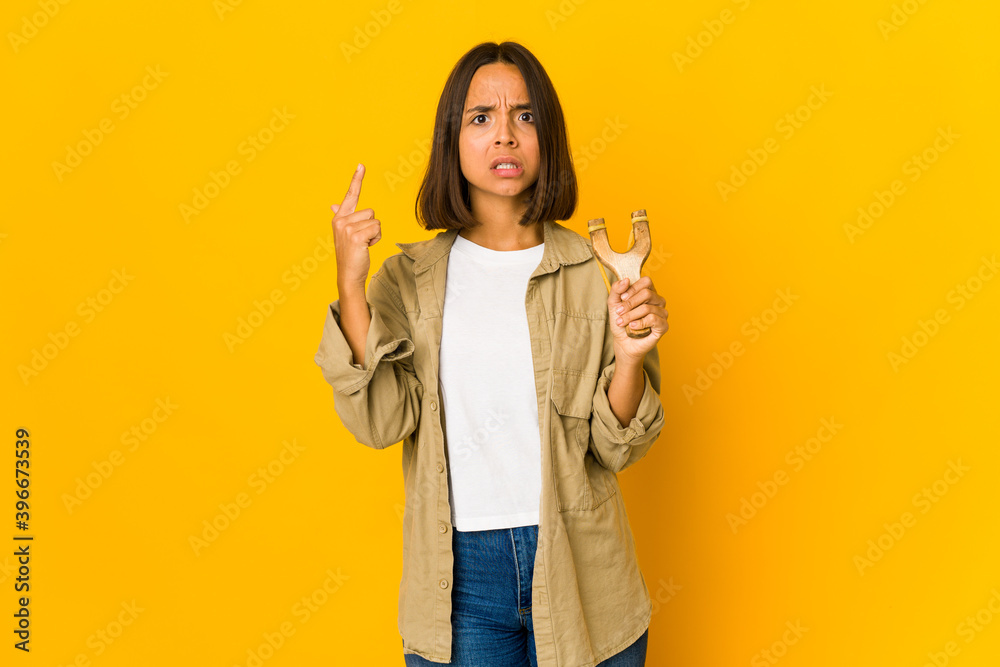 Young hispanic woman holding a slingshot showing a disappointment gesture with forefinger. Young hispanic woman holding a slingshot showing a disappointment gesture with forefinger.