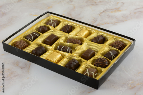 Open box of assorted Belgian chocolates in gold colored foil on table