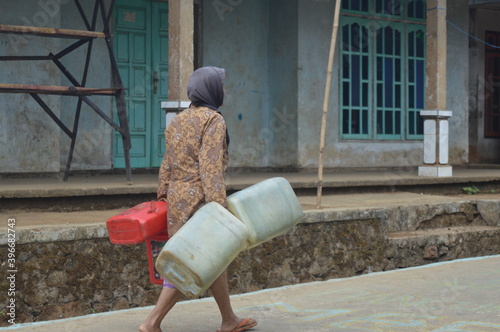 a mother is walking while carrying a jerry can filled with water in a village. The village experienced water shortages due to the long drought