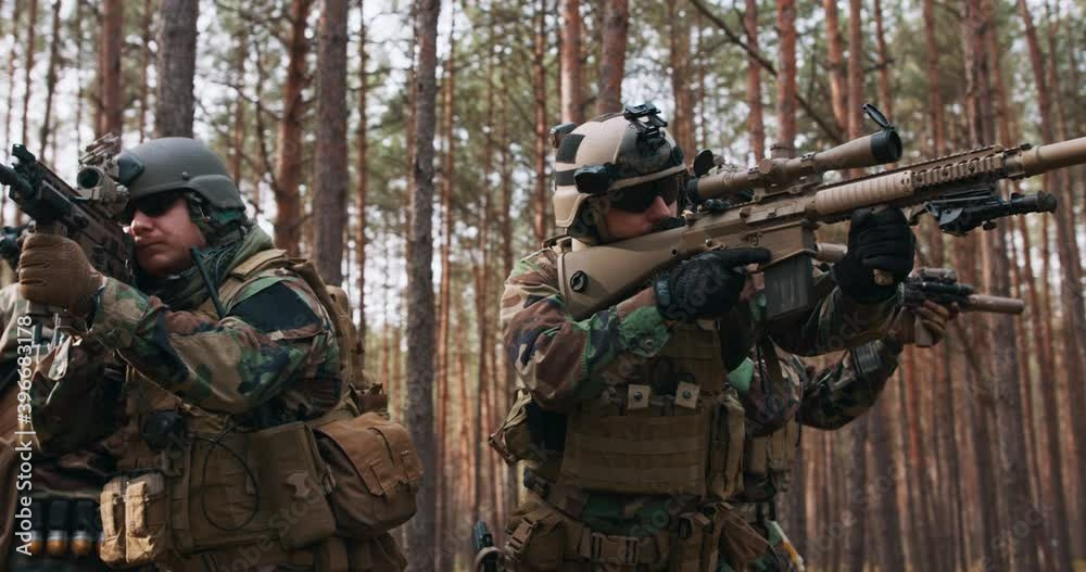 Four Fully Equipped Middle - Aged Soldiers Wearing Camouflage Uniform Attacking Enemy, They're in Shooting Ready Stance, Aiming Rifles. Military Operation in Action, Squad Standing in Dense Forest. Four Fully Equipped Middle - Aged Soldiers Wearing Camouflage Uniform Attacking Enemy, They're in Shooting Ready Stance, Aiming Rifles. Military Operation in Action, Squad Standing in Dense Forest.