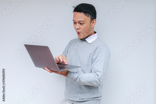 Young Asian man feeling happy and smile when standing and work laptop. Indonesian man wearing grey shirt