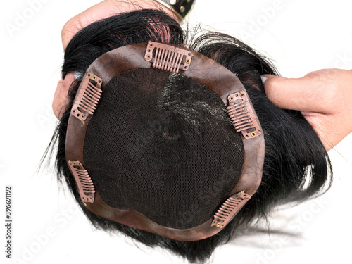 Holding a hair toupee or topper exposing the inside and showing the clips to help secure the hairpiece.
