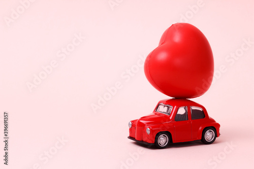 Valentines Day. Small red retro toy car with heart on the roof on pink background. New Year, Christmas, World Womans Day present delivery. Sale concept. Copy space.